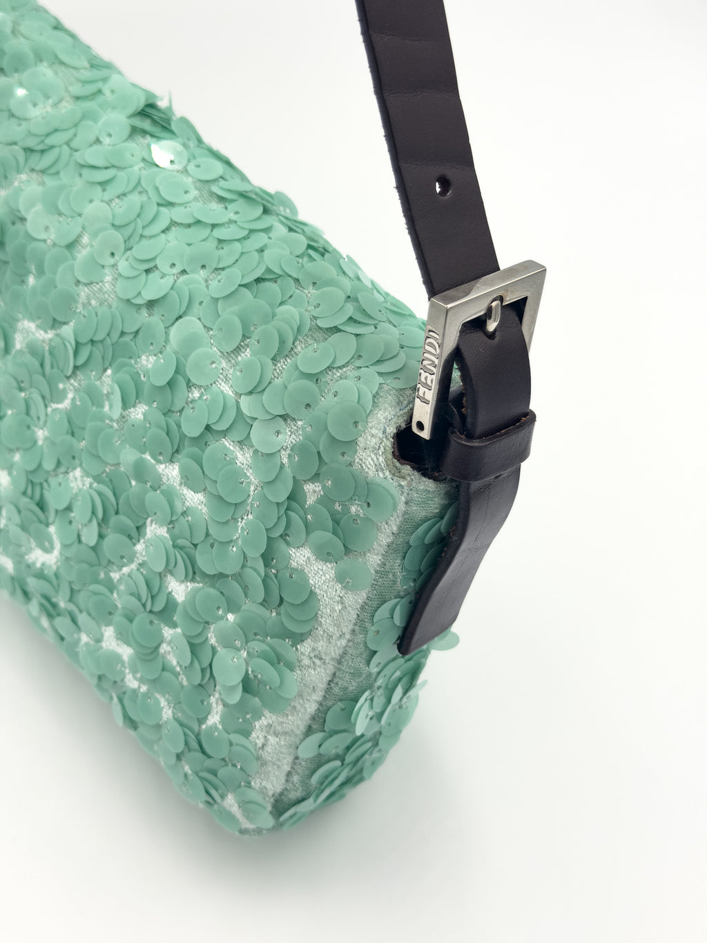 A close-up of a mint green sequined clutch bag with a black leather strap and silver-tone buckle on a white background.