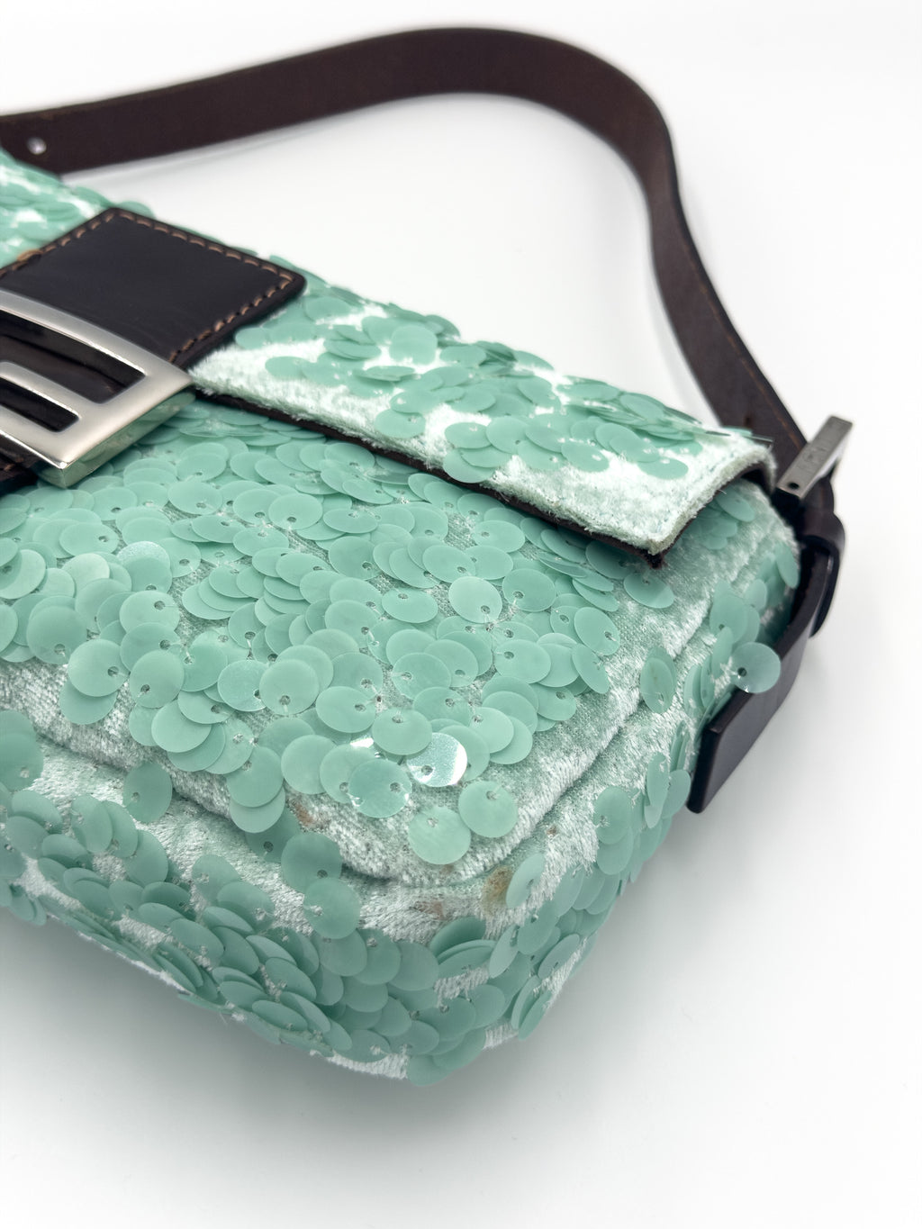 A mint green sequined shoulder bag with a dark brown leather strap and a silver-tone buckle, shown on a white background.